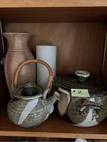 Shelf display: bamboo handled ceramic teapot, tall beige ceramic vase, short white ceramic vase, lidded ceramic casserole