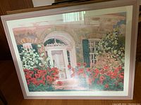Full view of the framed print showing a house entrance with lush red flowers in front.