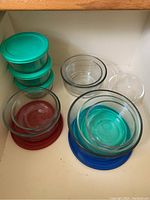 Top view of glass containers stacked with colored lids inside a cabinet drawer.