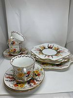 Photo showing 3 floral teacups stacked inside saucers with a stack of dessert and one larger plate behind, all decorated with multi-colored floral design and gold rims.
