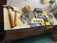 Photo showing multiple hand tools including two hammers, clamps, a rivet gun, tape measure, levels and other tools laid out on a table.