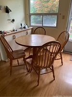 Oak harvest style dining table with four matching chairs arranged around it in a kitchen.
