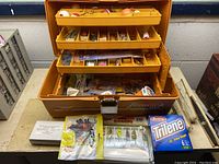 Open Fenwick 1080 fishing tackle box showing multiple tiered trays filled with various fishing bobbers, lures, hooks, and small tackle items