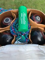 Overhead view showing four black lawn bowls with white and red rings, chamois container, and cloth inside carrying bag.