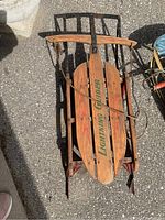 Top-down view showing the full sled with wooden seat slats and 'Lightning Guider' text, metal frame and runners visible.