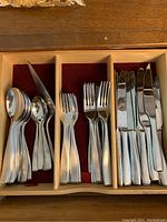 View of spoons, forks, and knives arranged in wooden holder with red velvet lining.