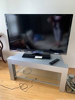 Sharp 48 inch flat-screen TV on gray stand with glass shelf and remote control on the stand