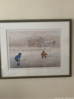 Full view of framed print showing two ice hockey players on a frozen pond with a rural house in background.