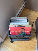 Black wheeled crate filled with multiple vinyl record albums visible from front and side, showing album cover of Harry Belafonte Calypso