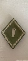 Diamond-shaped green Wedgwood dish with white relief of a figure holding a jug, surrounded by a white laurel leaf border.