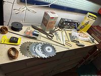 Overhead view of work bench showing circular saw blades, wire spools, a ratchet and socket driver, and various small hand tools spread out on surface