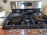 Four cast iron fry pans placed on a stove top, showing size variety and condition.