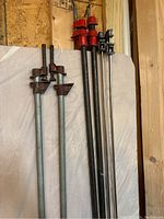 Image of long pipe clamps with red and silver colored components, standing vertically showing threaded tightening screws.
