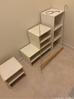 Four white shelving units of different sizes arranged against wall with belt/scarf hanger and double-hung rod