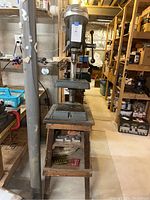 Front view of Craftsman drill press mounted on wooden stand in basement workshop.