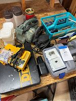 Overview of Dewalt drill case closed with charger and Quantum belt sander, sanding belts, small storage containers and vise grip on table.