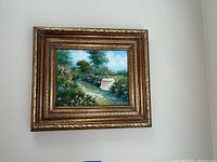 Framed oil painting hung on wall depicting garden scene with a white table under a tree in a lush garden