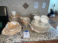 Wide shot of stacked Homer Laughlin Georgian china showing multiple stacks of plates, bowls, cups, and saucers arranged on granite countertop.