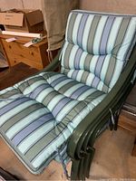 Four stacked green metal framed patio chairs with blue-green striped tufted cushions tied on. Cushions are thick and cover both seat and backrest.