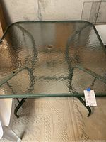 Full view of metal patio table with textured square glass top and metal frame.