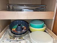 Shelf with stacked bakeware and kitchen items, including pie dishes, mixing bowls with lids, and bundt pan