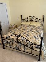 Full bed showing black metal frame with leaf design and floral bedding in beige and blue.