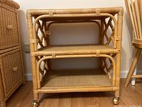 Front view of 2 shelf rattan rolling cart showing natural rattan material and woven shelf surfaces.