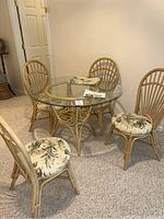 Full view of the rattan round glass top table with 4 rattan chairs with botanical fabric cushions.
