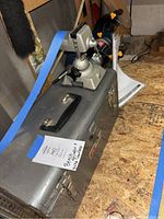 Craftsman metal toolbox with black handle and latch closures, labeled 'Bench Grndr + Misc Tools + Vise Grip'. Stored on a plywood surface.