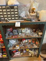 Wooden shelf with assorted screws, bolts, nuts, washers in small bags and packages on three shelves