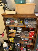 Wooden shelf unit holding multiple boxes and bins filled with assorted hardware items, fasteners, light bulbs, and tool packages.
