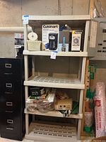 Full view of the 5 tier plastic shelving unit with various household items on some shelves, including a Cuisinart coffee maker box, paper towels, and other miscellaneous boxes and containers.