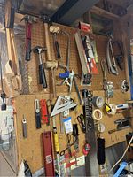 Full view of pegboard with many hand tools hanging including hammers, saws, squares, levels, scissors and measuring tools.