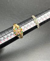 Two gold rings on ring sizer, one with diamond and emerald chips, the other plain, sizes 5.5-6 and 8