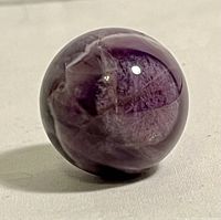 Polished amethyst sphere with visible cloudy inclusions and glossy finish on a neutral background.