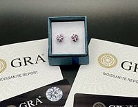 Pair of pink moissanite stud earrings in box with GRA certificates visible beneath.