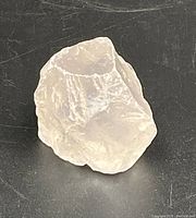 Photo of rough rose quartz gemstone showing translucent pale pink color and natural irregular surfaces.