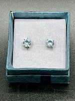 Blue topaz stud earrings displayed in a blue box with white padded insert, showing front view of stones and settings.