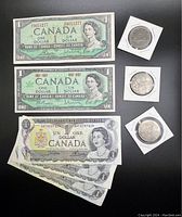 Collection of Canadian $1 banknotes and three $1 coins shown against a black background. Five banknotes total, four of one type and one of another, coins in protective holders.