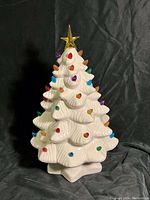 Full view of the white ceramic Christmas tree with colored bulb lights and star topper against black background, showing overall condition and design.