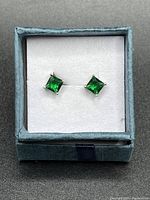 Front view of created emerald stud earrings in 925 silver presented in a blue box