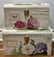 Stacked view of the two decorative storage trunks showing floral and vintage script pattern with metal latch closures