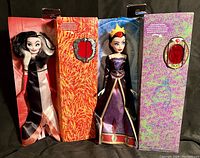 Two Disney Villains dolls (Cruella de Vil and Evil Queen) in their internal packaging with flame and mystical themed backgrounds and visible magic mirrors on the sides.