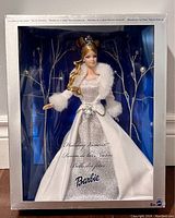 Front view of the boxed Barbie doll showing the full Winter Fantasy outfit including the sparkling silver front gown and white faux fur trimmed jacket, with visible tiara and elegant hairstyle.