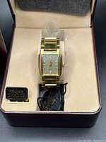 Close-up of Jules Jurgensen gold tone wristwatch inside presentation box showing face with two diamonds and metal bracelet.