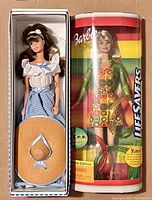 View of both dolls in their packaging side by side, showing the 1995 Little Debbie Barbie in a box and the 2000 Lifesavers Barbie in a cylindrical box with bracelets.
