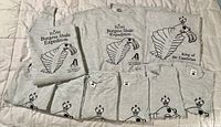 Seven gray ROM-themed T-shirts and two sweatshirts, all folded and laid out on a bedspread, showing black printed fossil/arthropod designs and text.