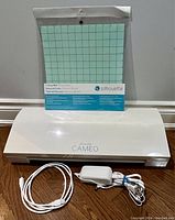 Silhouette Cameo 3 cutting machine, power adapter, USB cable, and brand new sealed 12 x 12 inch cutting mat packaged together.