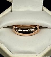 Front angled view of smooth polished rose gold tone silver ring in white jewelry box.