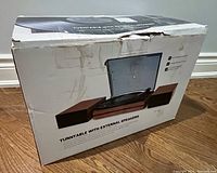 Photo of the outer packaging box showing the image of the turntable with external speakers and product title.